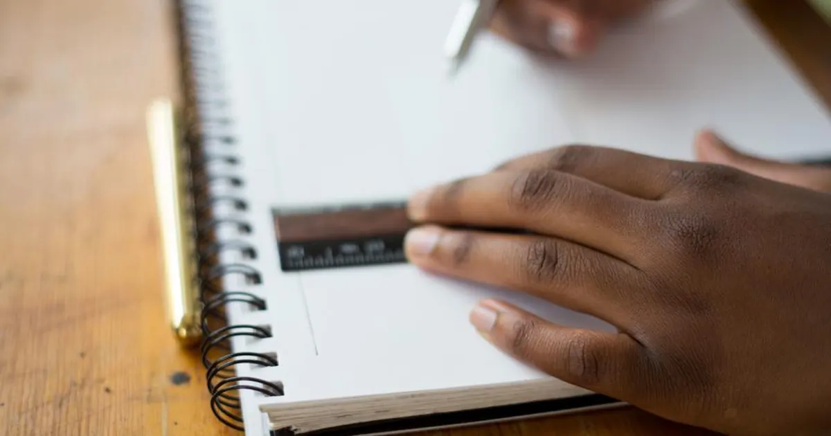 Student working through a past paper in a notebook with a ruler